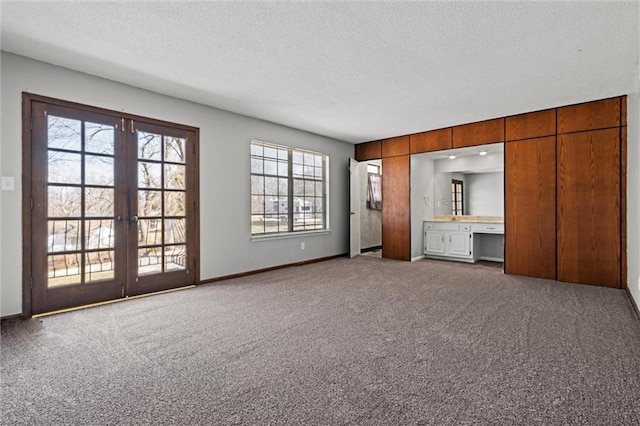 unfurnished living room with french doors, a textured ceiling, baseboards, and carpet floors