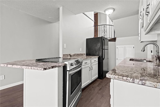 kitchen with a peninsula, freestanding refrigerator, a sink, electric stove, and white cabinetry