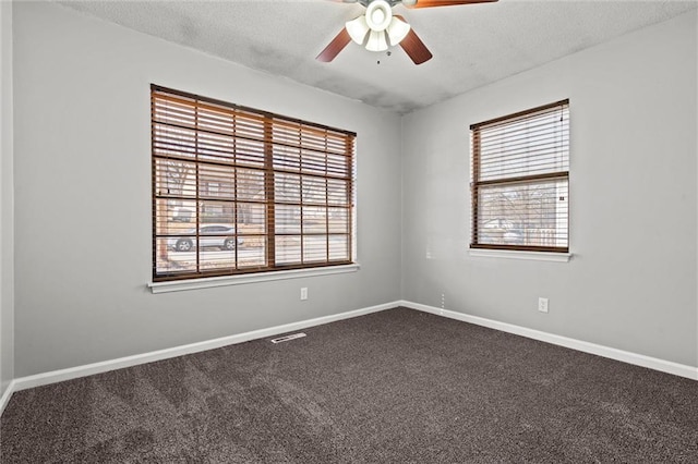 empty room featuring a textured ceiling, a ceiling fan, dark colored carpet, and a healthy amount of sunlight