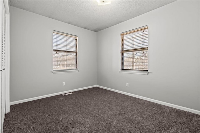 unfurnished room with dark colored carpet, visible vents, plenty of natural light, and a textured ceiling