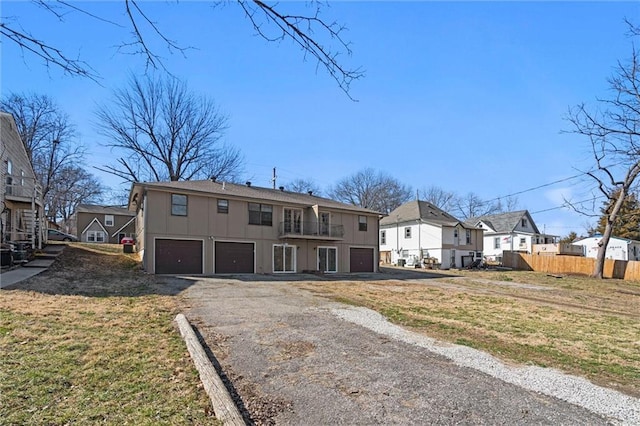 view of front of house featuring a balcony, fence, driveway, an attached garage, and a residential view