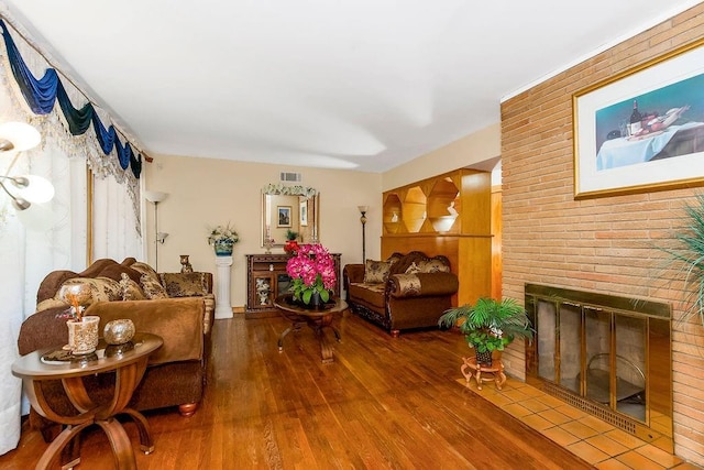 living area featuring a brick fireplace, wood finished floors, and visible vents