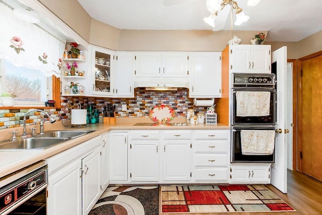 kitchen with backsplash, light countertops, white cabinets, black appliances, and a sink