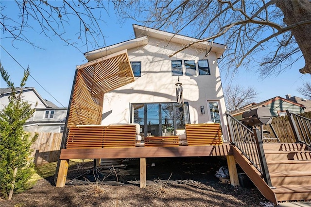 back of house with stucco siding, fence, and a wooden deck