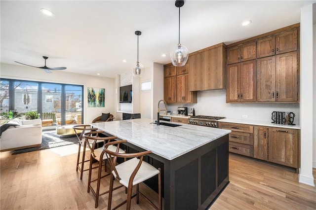 kitchen with custom exhaust hood, a sink, a kitchen bar, decorative light fixtures, and light wood-type flooring