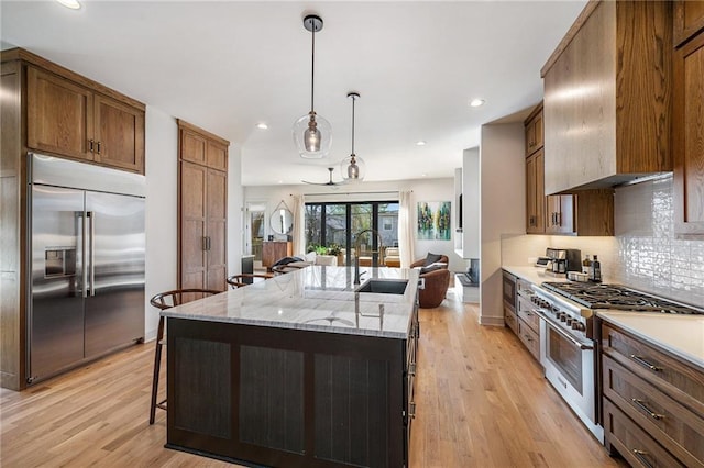 kitchen featuring premium range hood, light wood-style flooring, a sink, built in appliances, and tasteful backsplash