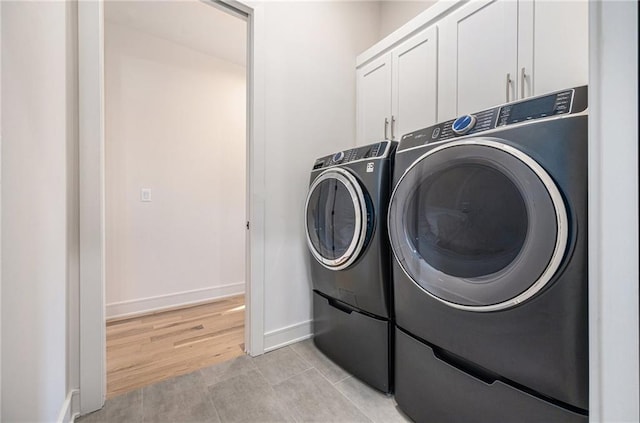 laundry area featuring baseboards, cabinet space, light wood-type flooring, and washing machine and clothes dryer