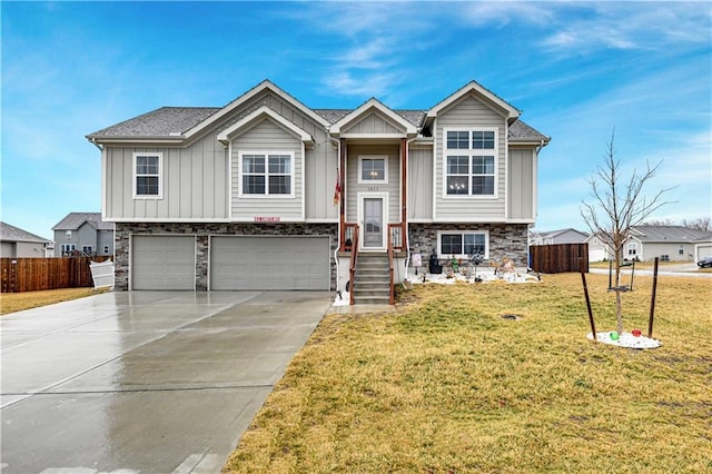 bi-level home featuring a garage, fence, concrete driveway, board and batten siding, and a front yard