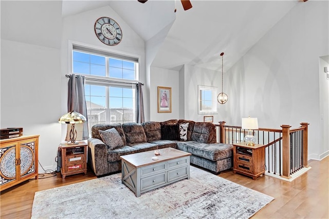 living area featuring light wood-style flooring, high vaulted ceiling, ceiling fan, and baseboards