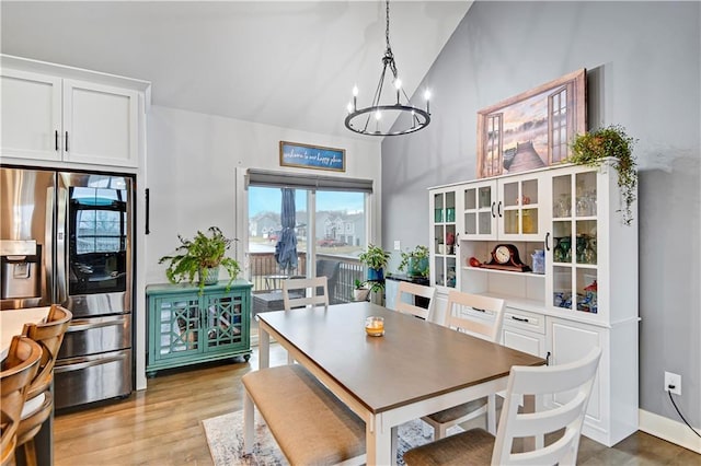 dining space with light wood-type flooring, an inviting chandelier, baseboards, and high vaulted ceiling