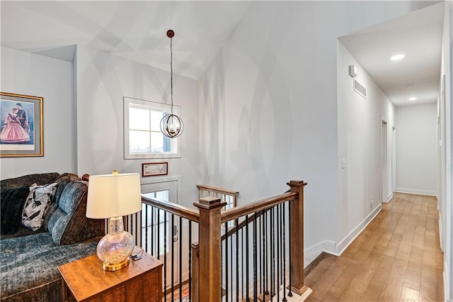 corridor with light wood-style flooring, a notable chandelier, visible vents, baseboards, and an upstairs landing