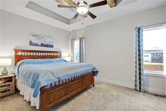 bedroom featuring light carpet, multiple windows, a raised ceiling, and baseboards