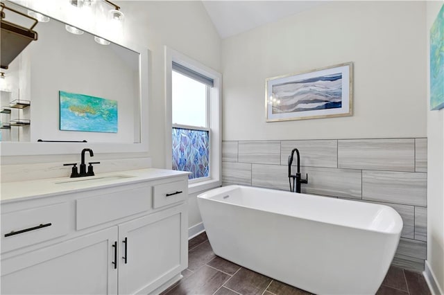 full bath featuring lofted ceiling, a freestanding bath, tile walls, and vanity