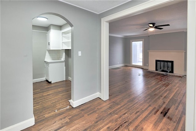 unfurnished living room with crown molding, dark hardwood / wood-style floors, ceiling fan, and a fireplace