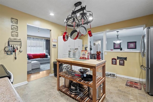 kitchen featuring stove, baseboards, light countertops, freestanding refrigerator, and pendant lighting