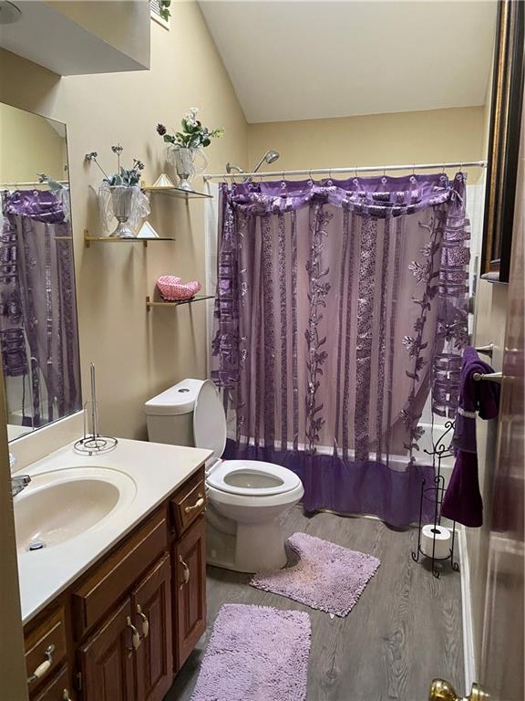 full bathroom featuring shower / bath combo, toilet, wood finished floors, vaulted ceiling, and vanity