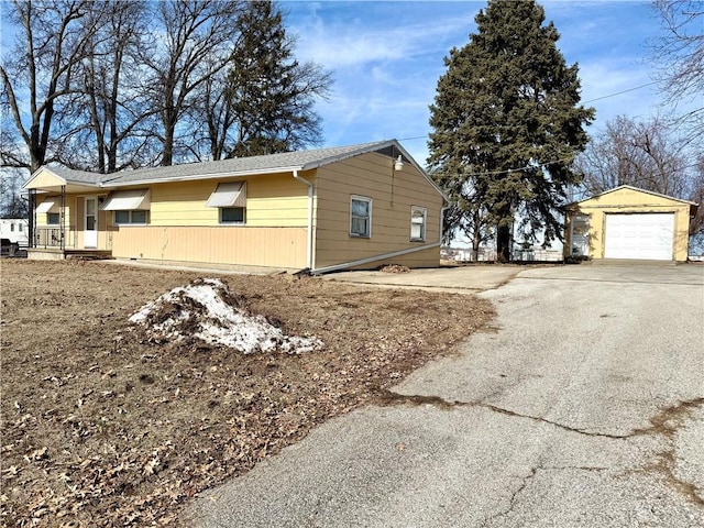 view of side of home featuring driveway, an outdoor structure, and a detached garage