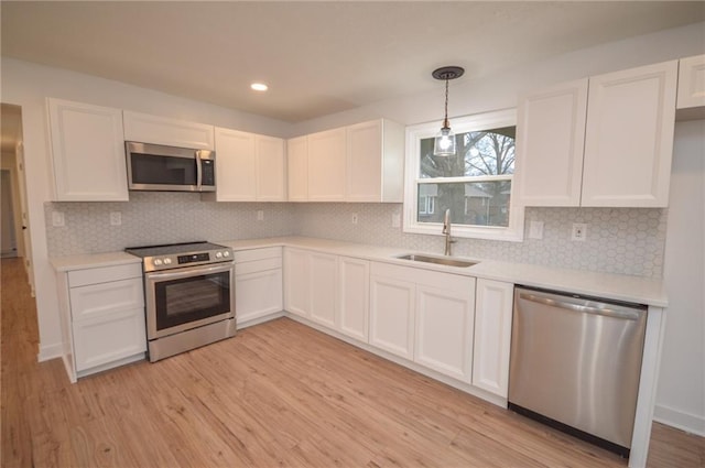 kitchen with pendant lighting, sink, white cabinetry, stainless steel appliances, and light wood-type flooring