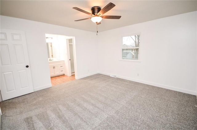 unfurnished bedroom with ensuite bathroom, light colored carpet, and ceiling fan