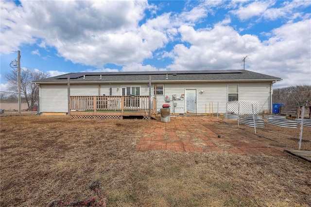 back of house with roof mounted solar panels, fence, and a wooden deck