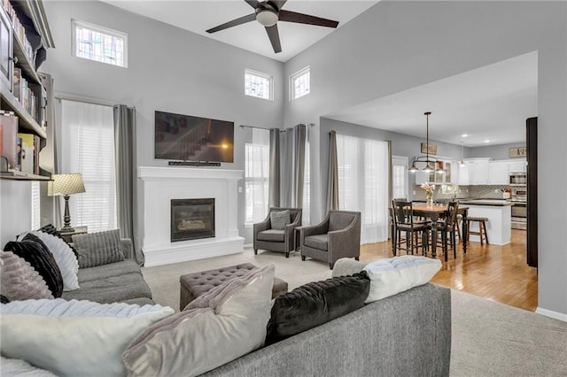 living area featuring ceiling fan, baseboards, a glass covered fireplace, and light colored carpet