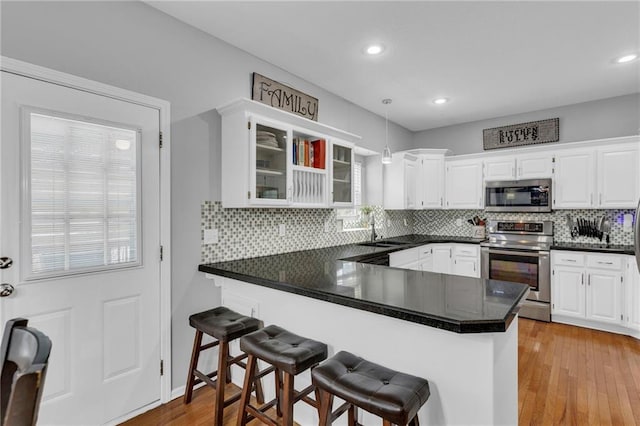 kitchen with a peninsula, appliances with stainless steel finishes, white cabinets, and a sink