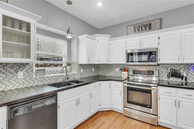 kitchen featuring dark countertops, appliances with stainless steel finishes, light wood-style floors, white cabinetry, and a sink