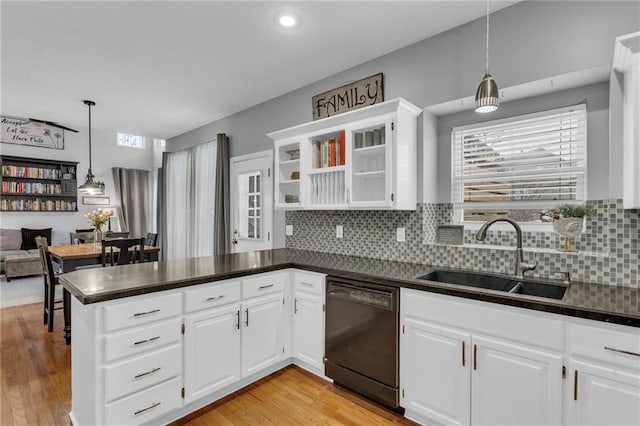 kitchen with a peninsula, a sink, dishwasher, light wood finished floors, and dark countertops