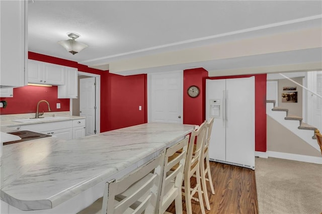 kitchen with white refrigerator with ice dispenser, a kitchen breakfast bar, a peninsula, white cabinetry, and a sink