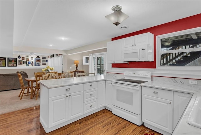 kitchen with a peninsula, white appliances, white cabinetry, and light wood finished floors