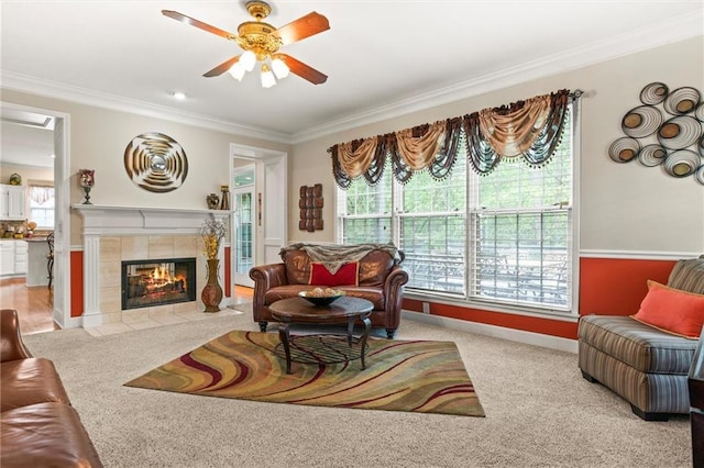 carpeted living room with a tiled fireplace, ornamental molding, and ceiling fan