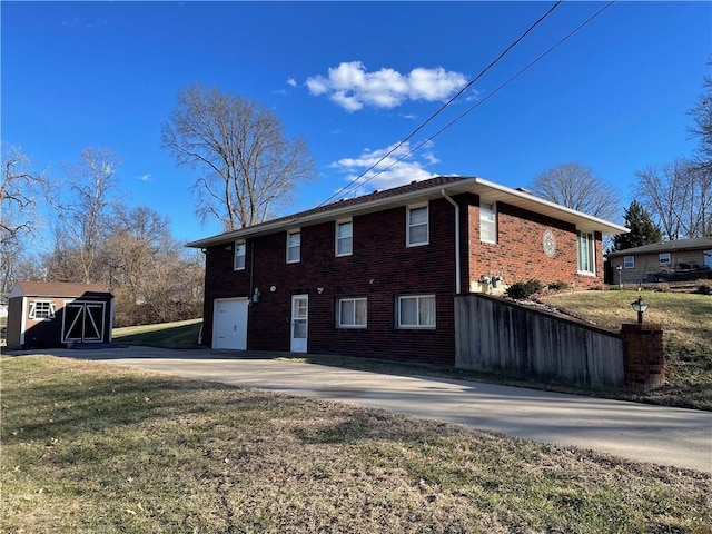 back of house featuring concrete driveway, a yard, an outbuilding, and brick siding