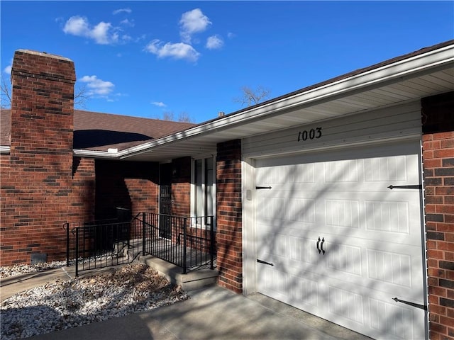 entrance to property featuring a garage, a chimney, concrete driveway, and brick siding