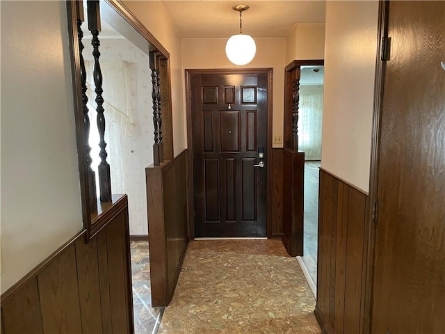 doorway featuring stone finish flooring, a wainscoted wall, and wood walls