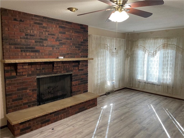 unfurnished living room featuring baseboards, visible vents, wood finished floors, a textured ceiling, and a brick fireplace