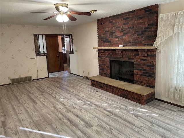 unfurnished living room with visible vents, a brick fireplace, wood finished floors, baseboards, and wallpapered walls