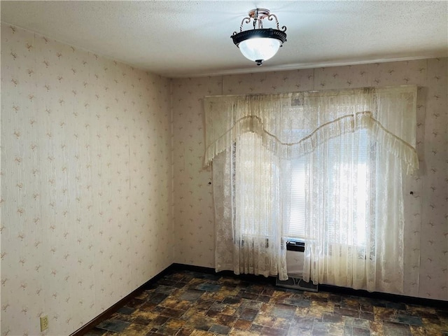 unfurnished room featuring a textured ceiling, baseboards, and wallpapered walls