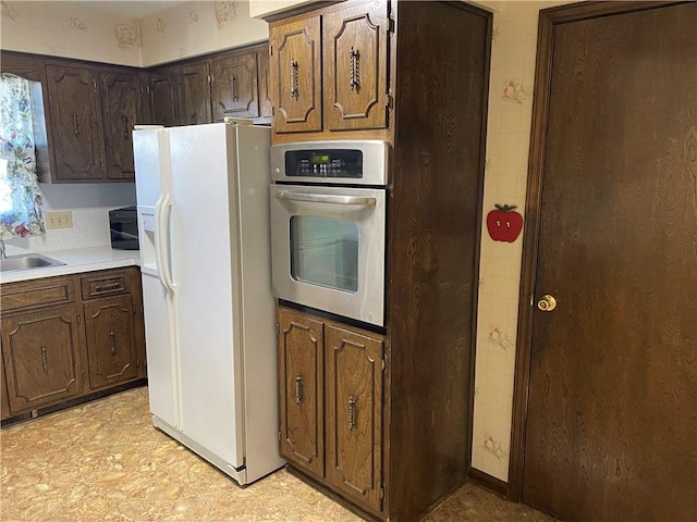 kitchen featuring dark brown cabinetry, light countertops, white fridge with ice dispenser, stainless steel oven, and a sink