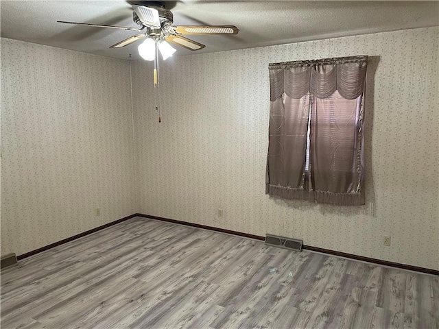 empty room featuring wood finished floors, visible vents, and wallpapered walls