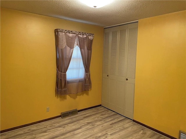 unfurnished bedroom with a closet, visible vents, light wood-style flooring, a textured ceiling, and baseboards