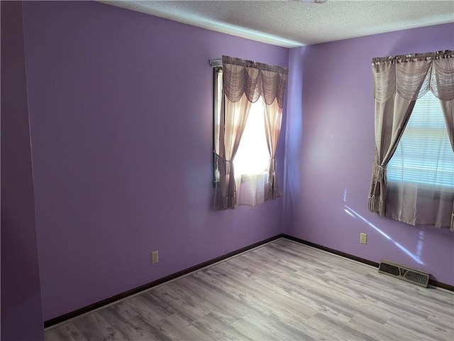 empty room featuring a textured ceiling, wood finished floors, visible vents, and baseboards