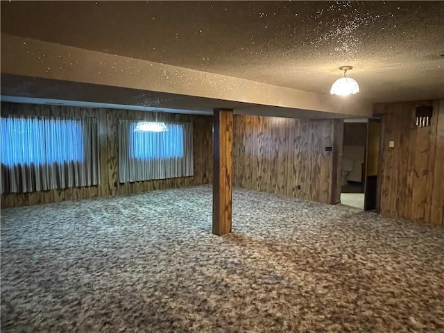 finished basement featuring a textured ceiling, wood walls, and carpet flooring