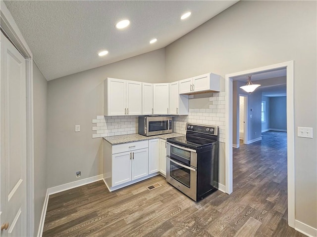 kitchen with dark wood-type flooring, vaulted ceiling, appliances with stainless steel finishes, white cabinets, and backsplash