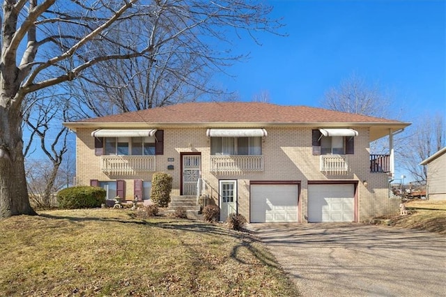 bi-level home with an attached garage, a front yard, aphalt driveway, and brick siding