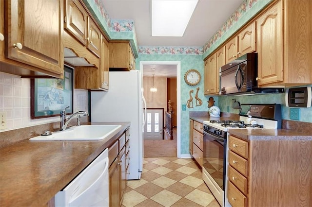 kitchen with light floors, a sink, white appliances, baseboards, and wallpapered walls