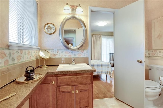 bathroom with toilet, wallpapered walls, and vanity