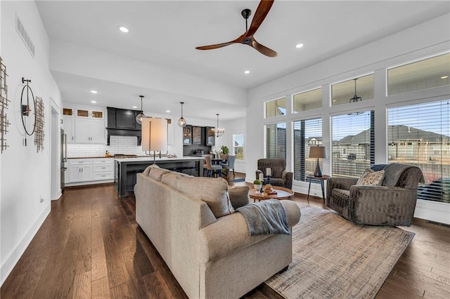 living room featuring recessed lighting, ceiling fan with notable chandelier, visible vents, baseboards, and dark wood-style floors