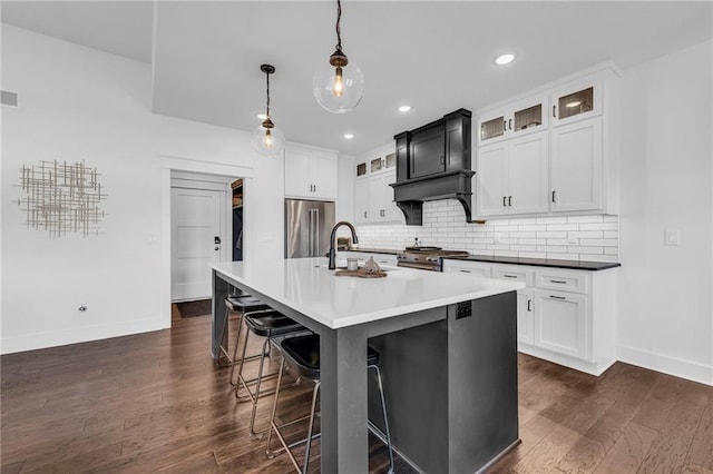 kitchen featuring decorative light fixtures, high end appliances, dark countertops, glass insert cabinets, and an island with sink