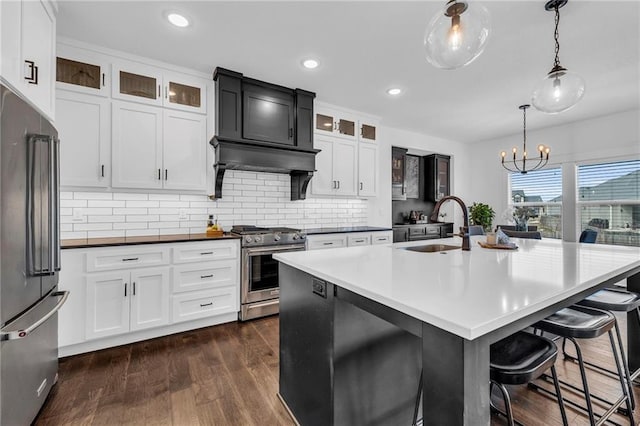 kitchen featuring glass insert cabinets, hanging light fixtures, an island with sink, and high quality appliances