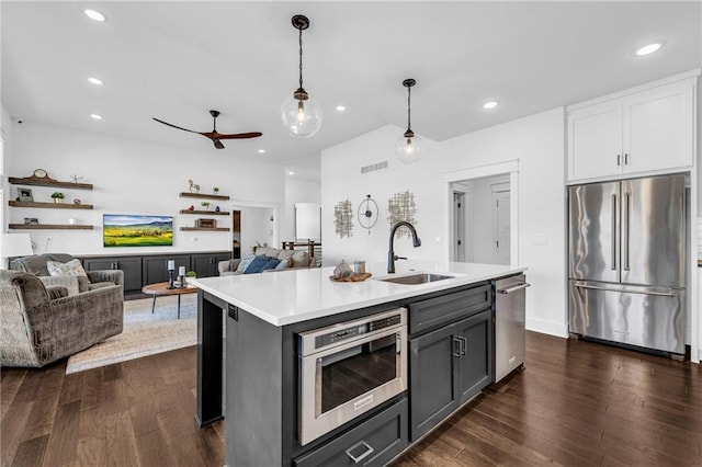 kitchen featuring appliances with stainless steel finishes, open floor plan, a kitchen island with sink, light countertops, and a sink